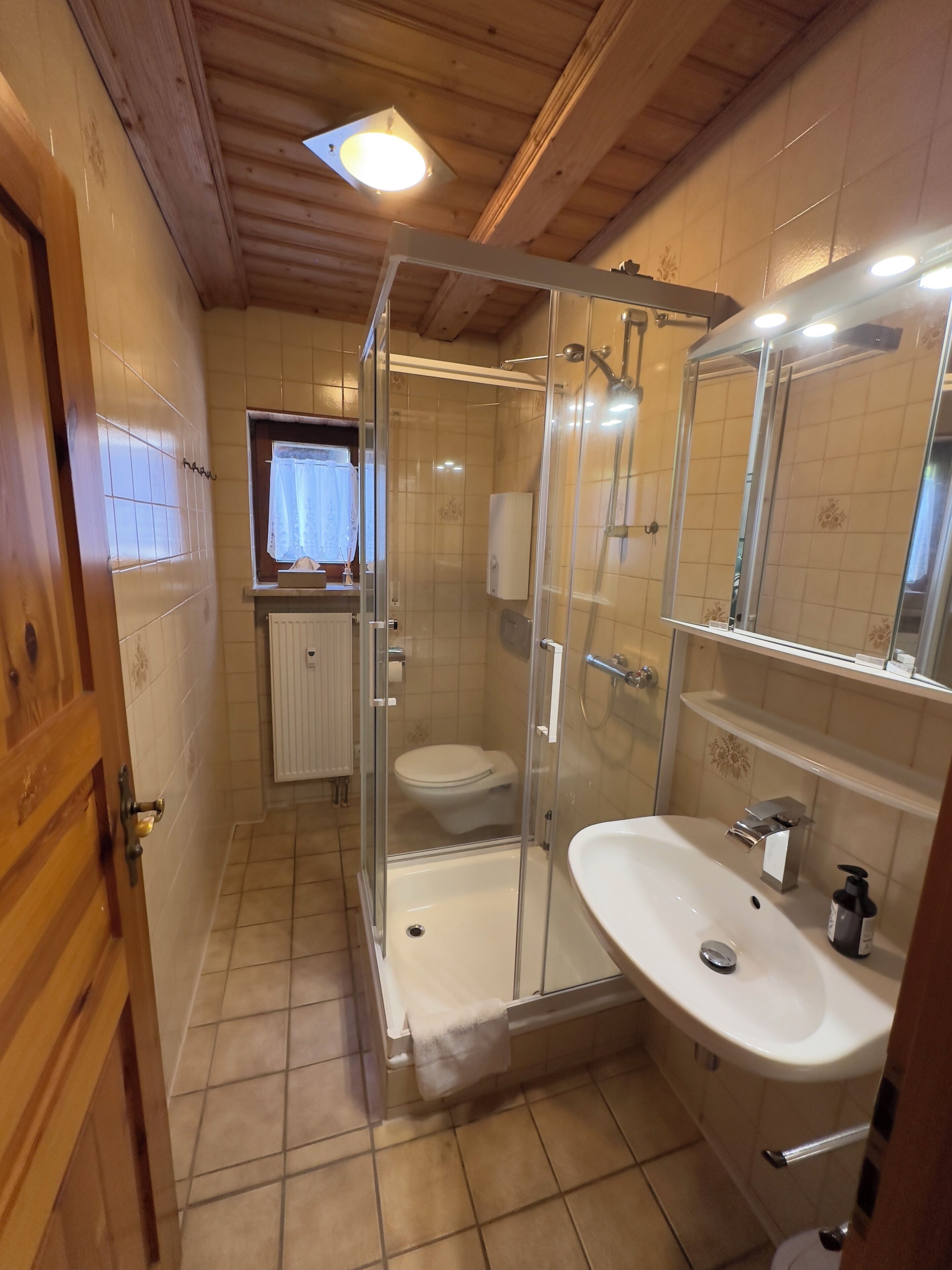 Ein Badezimmer mit Duschkabine, Toilette, Waschbecken und einem Fenster mit Vorhang.