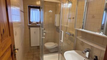 Ein Badezimmer mit Duschkabine, Toilette, Waschbecken und einem Fenster mit Vorhang.