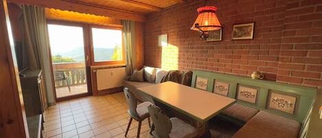 A cozy dining area with a wooden table and benches, a brick wall, and a view through a window.