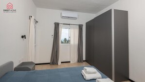 Een hotelkamer met een bed, twee handdoeken, een kledingkast, een raam met gordijnen en een airconditioning.