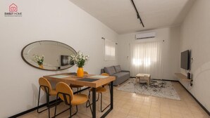 Een moderne woonkamer met een eethoek, een grijze bank, een televisie en een grote spiegel.