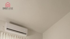 Een kamer met een houten tafel, een wandairconditioning, een groot raam met witte gordijnen en een schilderij aan de muur.