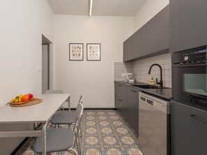 Eine kleine Küche mit Esstisch, Stühlen, Kühlschrank und Geschirrspüler. An der Wand befinden sich zwei gerahmte Bilder.