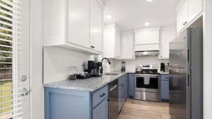 A modern kitchen with white cabinets, a granite countertop, stainless steel appliances, and a wooden floor.