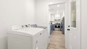 A laundry area with a front-loading washer and dryer, a kitchen with modern appliances, and a hallway leading to a door with a window.