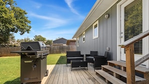 A deck with outdoor furniture, a grill, and a staircase leading to a house.