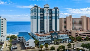 A high-rise hotel with multiple floors, a central tower, and a beach view.