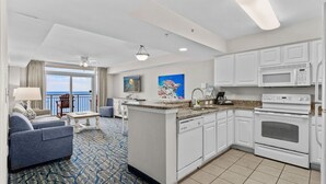 A modern hotel room with a kitchenette, a dining area with a view, and a living area with a sofa and a coffee table.