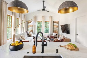 Eine moderne Küche mit Marmorarbeitsplatte, einem schwarzen Wasserhahn und einer Zitronenschale. Ein Holztisch mit einer Flasche und einem Schneidebrett mit Brot und Trauben.