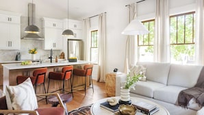 Une cuisine moderne avec des meubles blancs, un îlot central doté de tabourets de bar et un coin repas comprenant un canapé et une table basse.