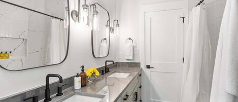 Un baño moderno con lavamanos doble, un espejo grande y zona de ducha.