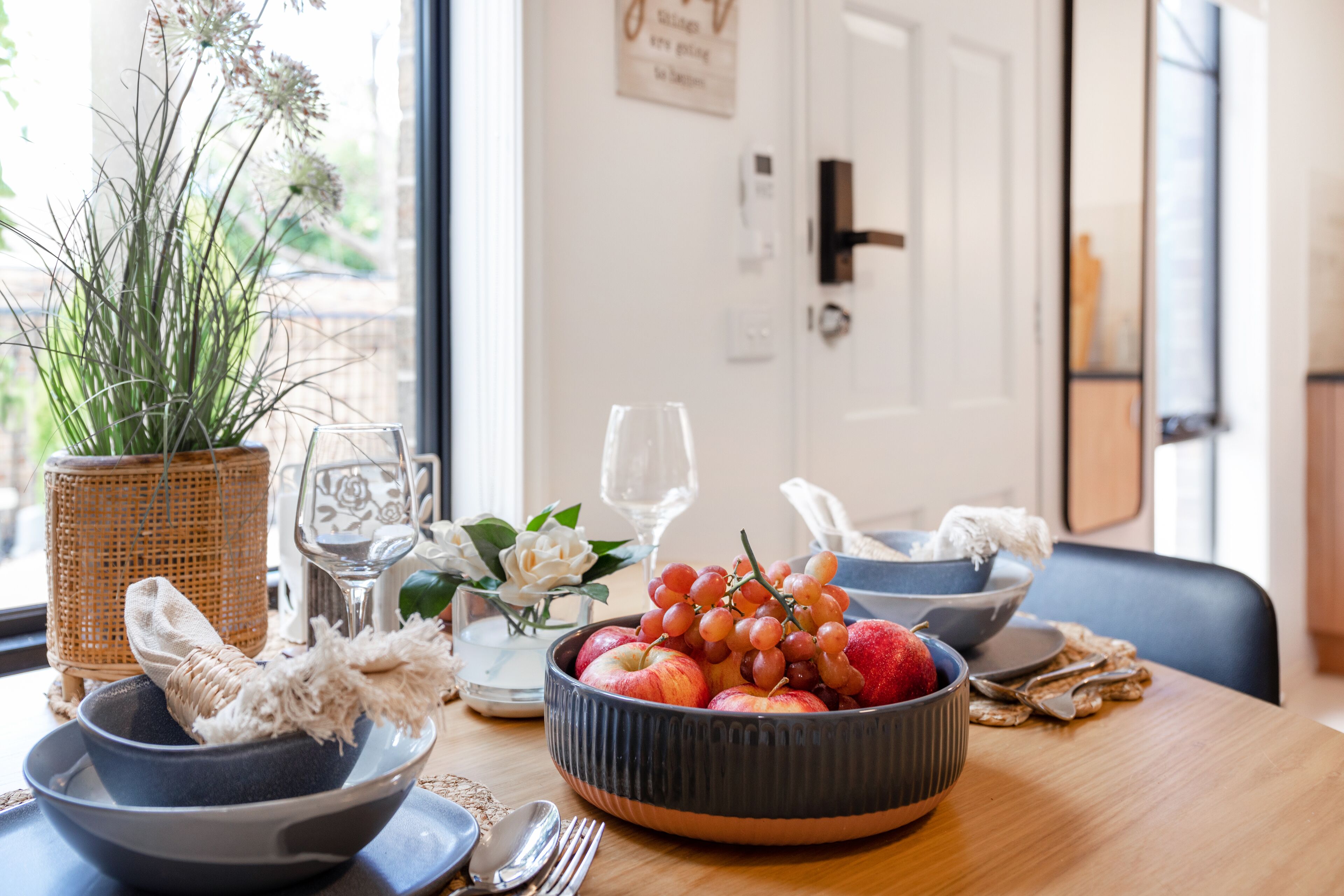 A dining table with a fruit bowl, a woven basket, and a vase with flowers.