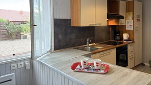 A compact kitchen with wooden cabinets, a built-in stove, and a window with a view of a garden. - Cottage with covered pool in Auvergne (Le Theil)