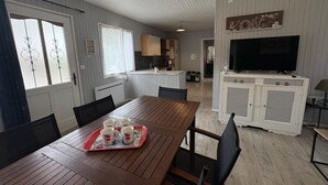 A dining area with a wooden table, chairs, and a tray with cups. There is a kitchen area with cabinets and a TV. - Cottage with covered pool in Auvergne (Le Theil)
