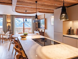 Cozinha moderna com bancada de mármore, cadeiras de madeira e iluminação pendente.