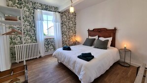 A bedroom with a wooden bed, white bedding, a radiator, a wooden nightstand with a lamp, and a shelf with a basket. - Charming and Comfortable Cottage in Saint-Haon-le-Châtel, Pets Allowed (Saint-Haon-le-Châtel)