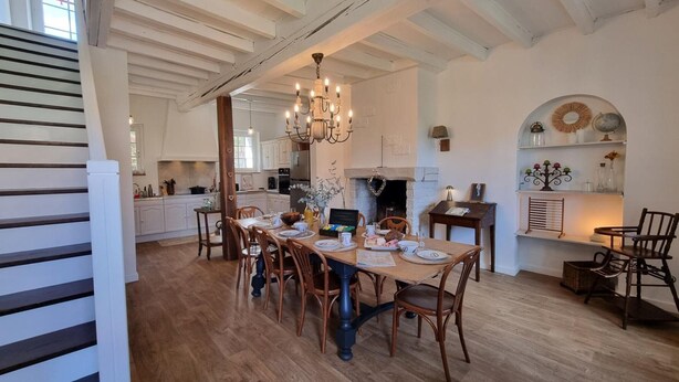 A spacious dining area with a wooden table set for six, surrounded by wooden chairs. A chandelier hangs above, and a fireplace is visible in the background. - Charming and Comfortable Cottage in Saint-Haon-le-Châtel, Pets Allowed (Saint-Haon-le-Châtel)