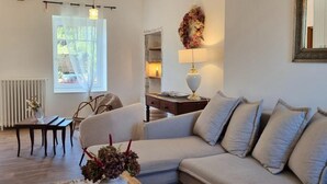 A living room with a sofa, a table with a vase, a lamp, and a window with curtains. - Charming and Comfortable Cottage in Saint-Haon-le-Châtel, Pets Allowed (Saint-Haon-le-Châtel)