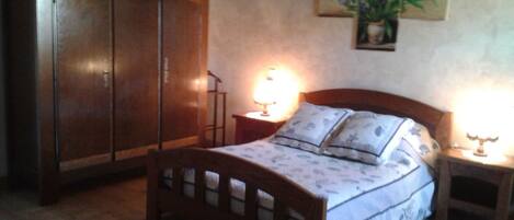 A bedroom with a wooden bed, two bedside tables, a nightstand, a wardrobe, and a chandelier.