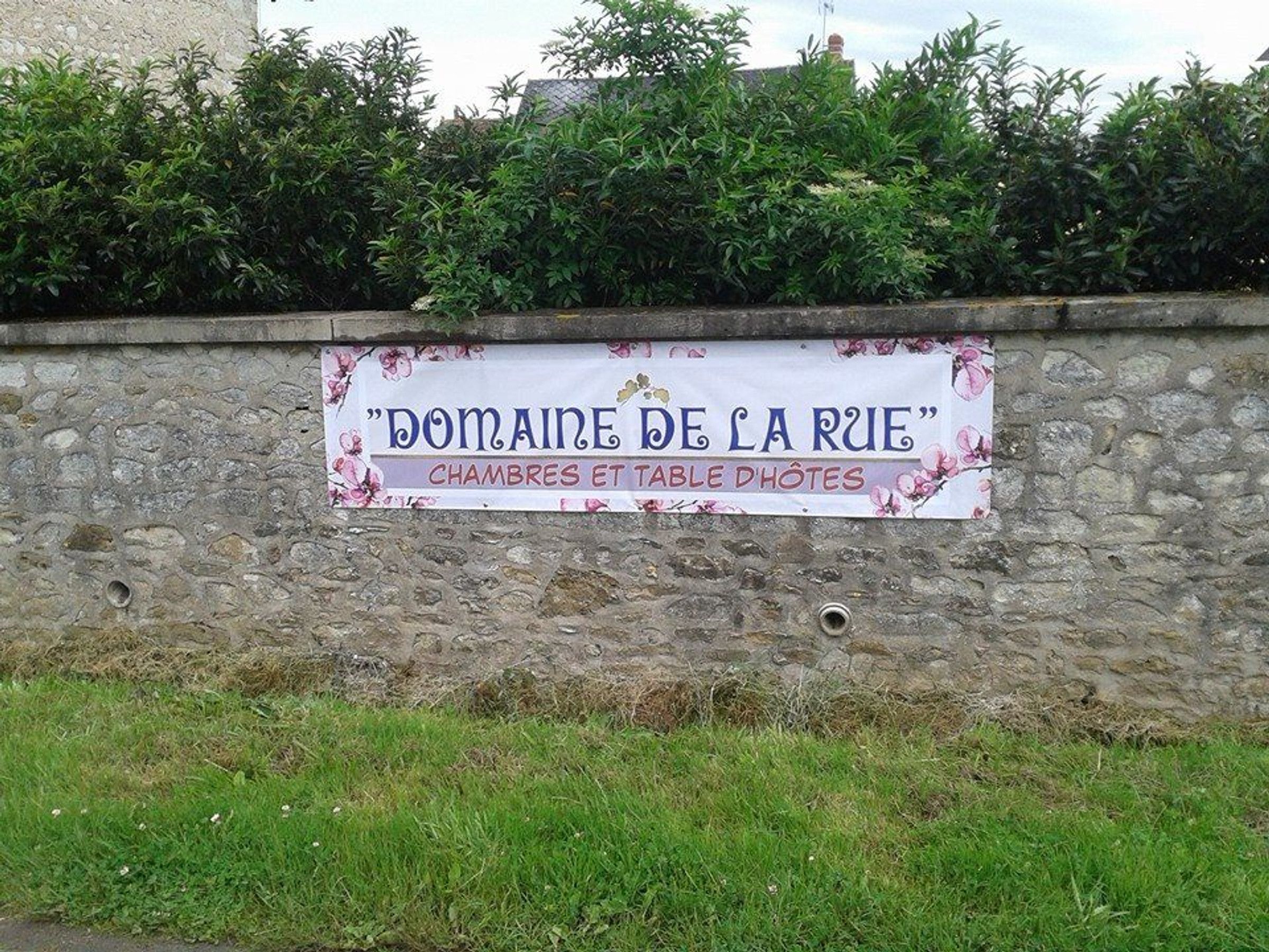 A stone wall with a sign that reads "Domaine de la Rue" and mentions "chambres et table dhotes".