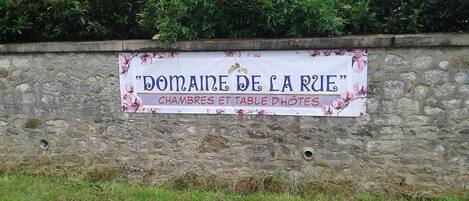 A stone wall with a sign that reads "Domaine de la Rue" and mentions "chambres et table dhotes".