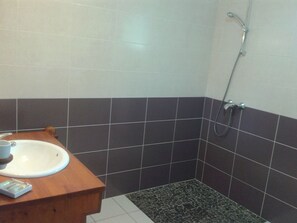 Un baño con lavamanos blanco, paredes de azulejos oscuros y zona de ducha.