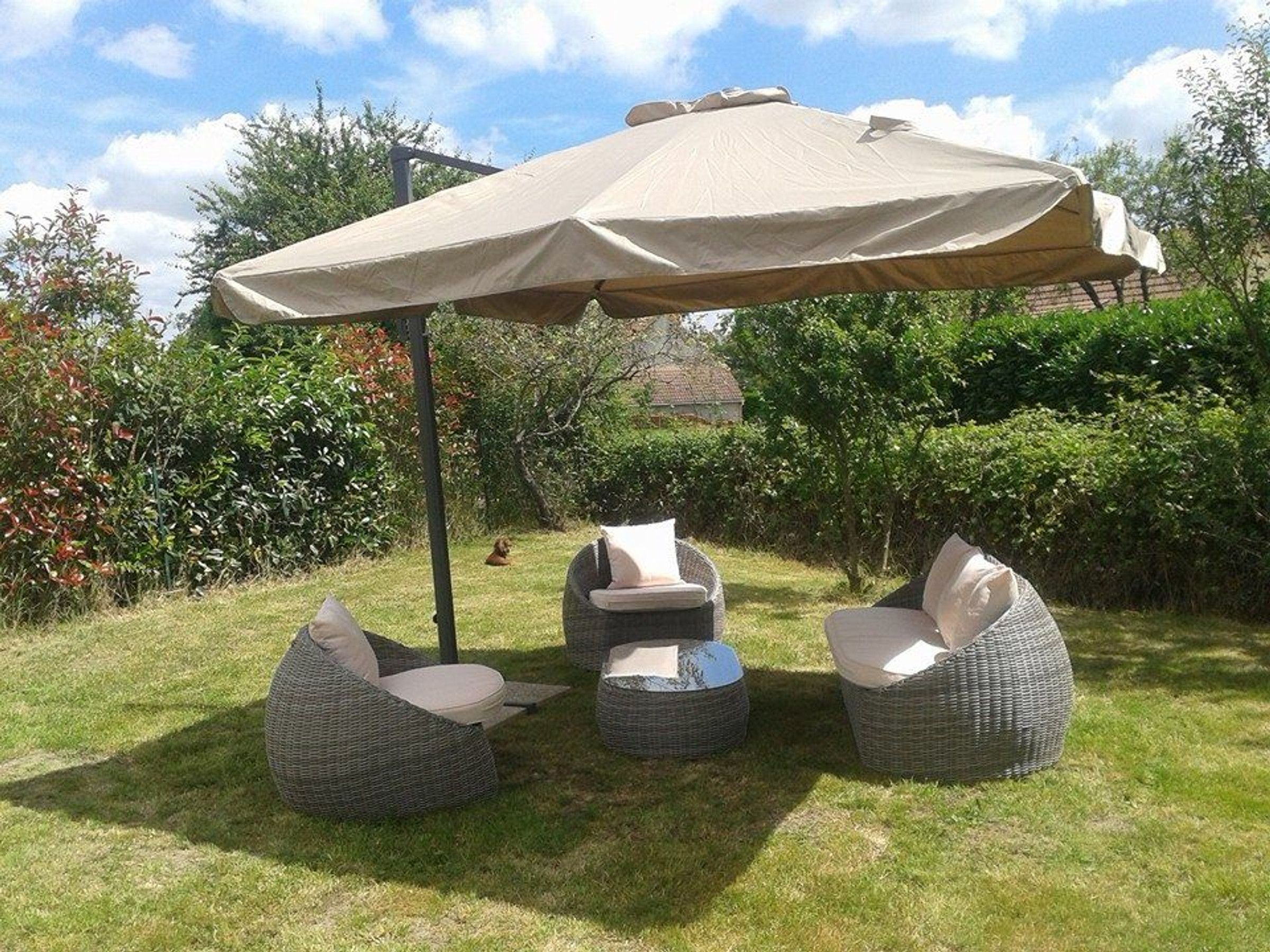 Un espace patio agrémenté d’un grand parasol, de chaises en osier et d’une table ronde.