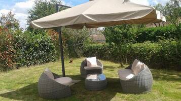 Un espace patio agrémenté d’un grand parasol, de chaises en osier et d’une table ronde.