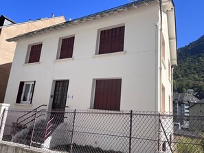 A building with a white facade, multiple windows with brown shutters, and a metal fence in the foreground. - Charming apartment in Cauterets with views and parking (Cauterets)