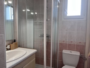 Un baño con cabina de ducha de vidrio, inodoro blanco y lavabo con espejo superior.