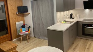 A compact kitchen with a built-in oven, a sink, and a small dining area with a table and chair. - Studio cabin for 4 people, 3* with NW facing balcony (Valloire)