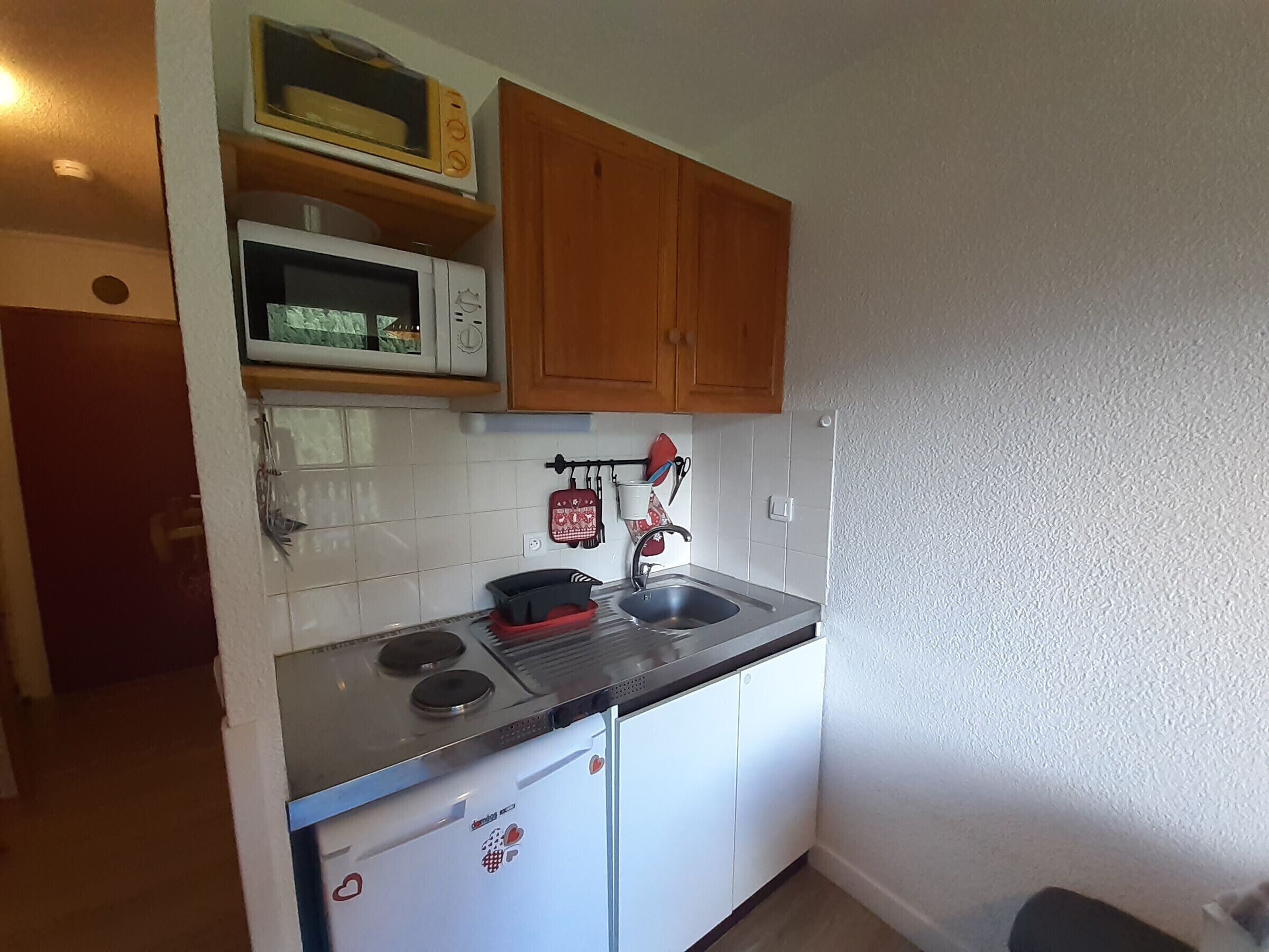 A compact kitchen with a microwave, stove, sink, and wooden cabinets.