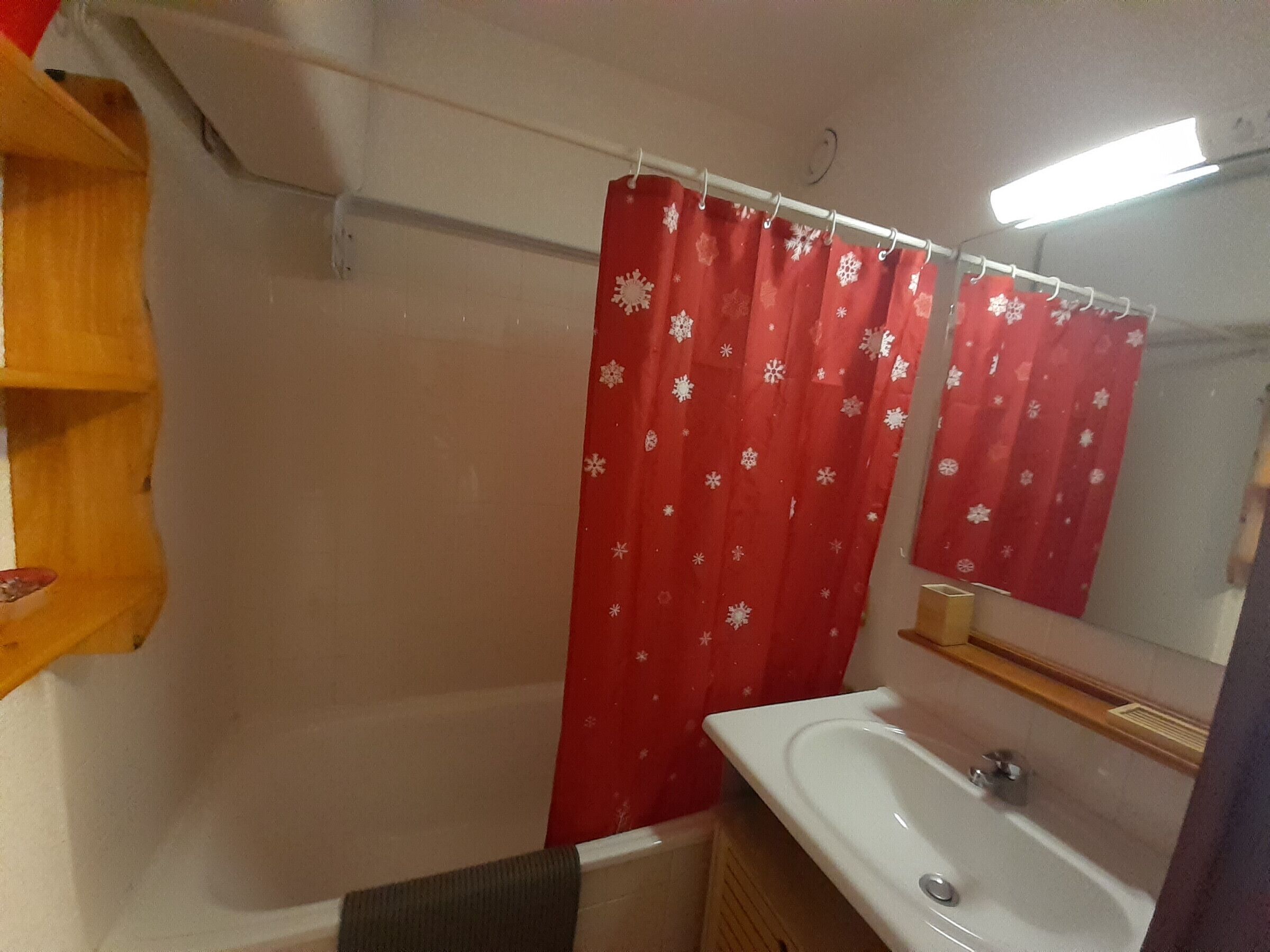 Een badkamer met een wit wastafeltje, een spiegel en een rood douchegordijn met sneeuwvlokmotieven.