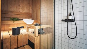 A sauna with wooden benches, a small table with a towel, a black container, and a glass-enclosed steam room.