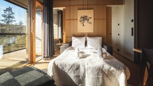 A modern bedroom with a large bed, a wooden slatted ceiling, and a sliding glass door leading to a balcony.