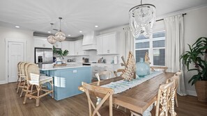 Una cocina moderna con armarios blancos, una isla azul, sillas de mimbre y una araña.