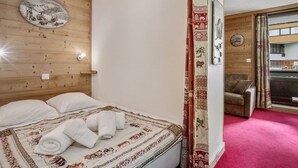 Een kamer met een houten hoofdeinde, een bed met een bedspread met patroon, een wandklok en uitzicht op een balkon met een stoel.