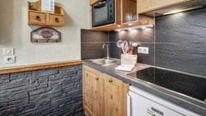 Een compacte keuken met houten kastjes, een magnetron, een fornuis en een betegelde achterwand.