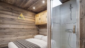 A wooden cabin-style room with a bed, a shower with a glass enclosure, and a wooden cabinet.