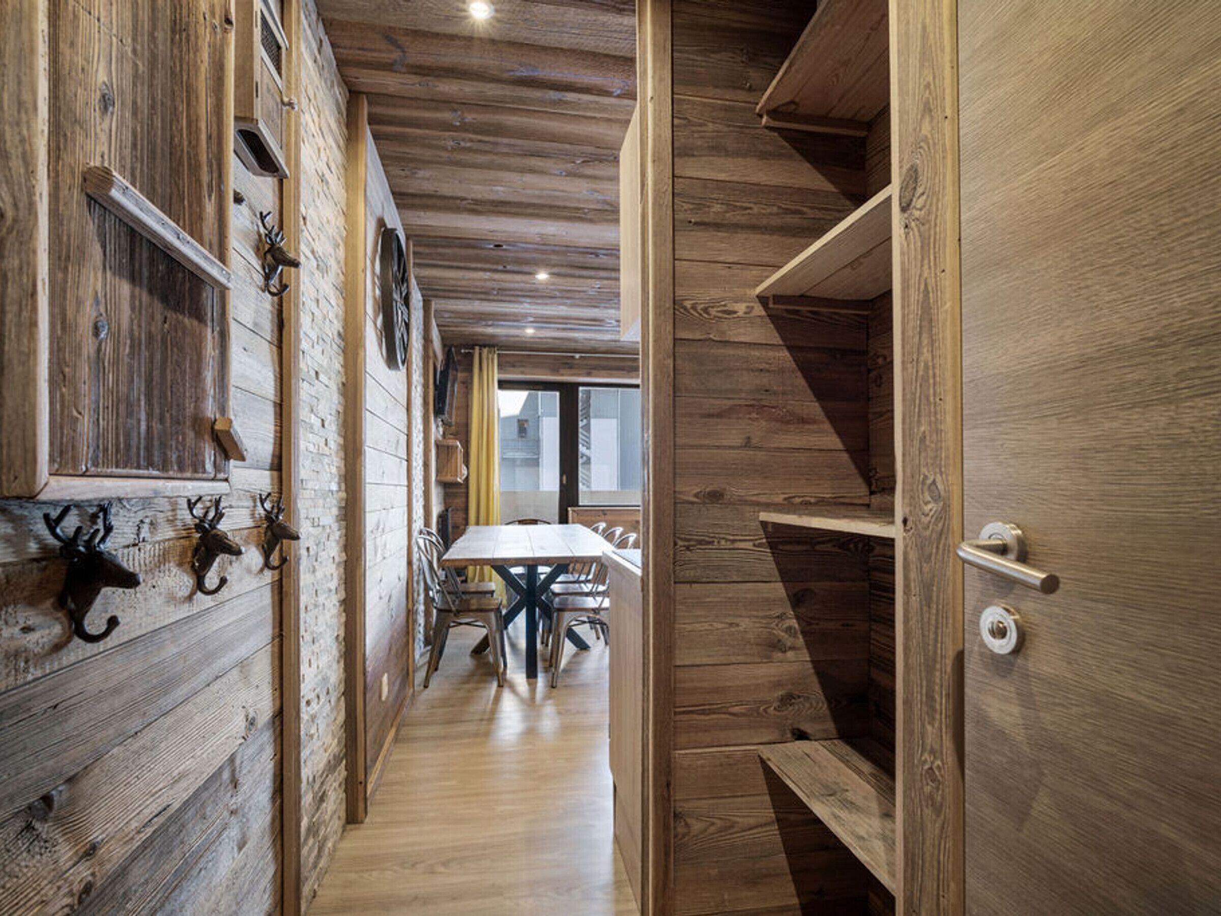 A narrow hallway with wooden walls and ceiling, leading to a dining area with a table and chairs.