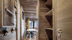A narrow hallway with wooden walls and ceiling, leading to a dining area with a table and chairs.