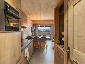 A modern kitchen with wooden cabinets, a dining area with chairs, and a view of mountains through a large window. - Duplex for 6, central location, balcony and pets allowed (Val Thorens)