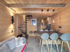 A modern interior with a wooden floor, a sofa, a dining table with chairs, a kitchen area, and a staircase. - Duplex for 6, central location, balcony and pets allowed (Val Thorens)