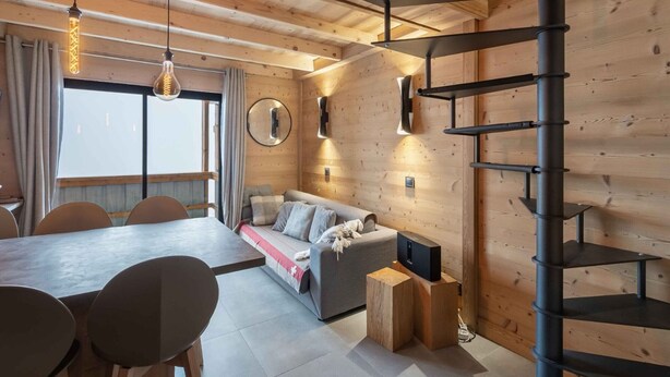 Een modern interieur met een houten plafond, een eetgedeelte met een lange tafel en stoelen, een bank met kussens, een televisie op een houten dressoir, en een wenteltrap.