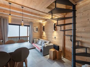 A modern interior with a wooden ceiling, a dining area with a long table and chairs, a sofa with cushions, a TV on a wooden stand, and a spiral staircase. - Duplex for 6, central location, balcony and pets allowed (Val Thorens)