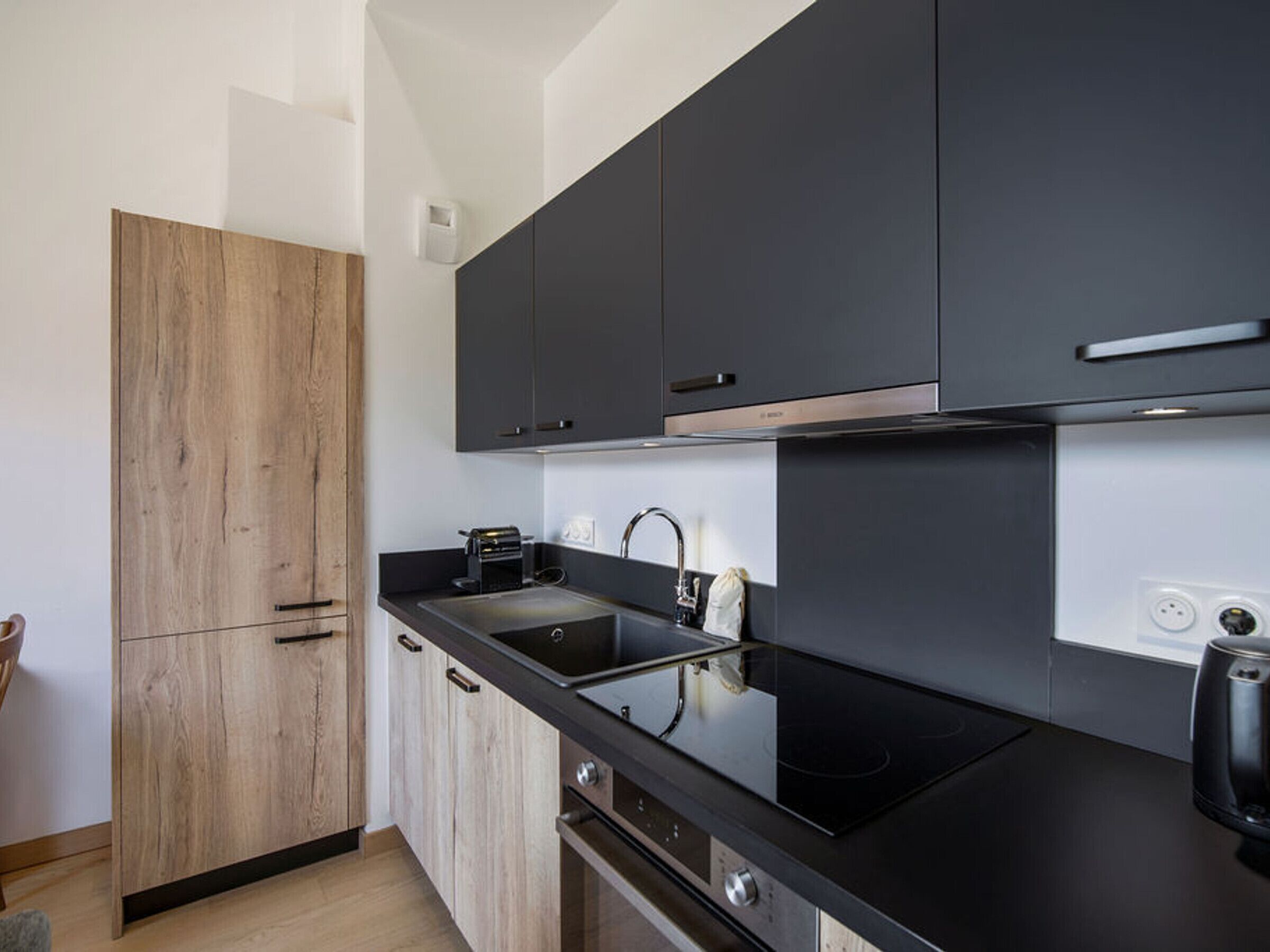 Una cucina moderna con mobili scuri, un armadio in legno, un piano di lavoro nero, un fornello e un lavandino.