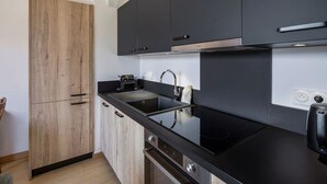 A modern kitchen with dark cabinets, a wooden cabinet, a black countertop, a stove, and a sink.