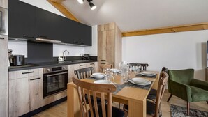 A modern kitchen with dark cabinets, wooden beams, and a dining area with a table set for four. - Comfort and Quiet in Nantailly, T3 for 6 pers. (Les Saisies)