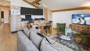 A modern living room with a grey sofa, a dining area with a wooden table and chairs, a kitchen with black cabinets and a microwave, and a television on the wall. - Comfort and Quiet in Nantailly, T3 for 6 pers. (Les Saisies)