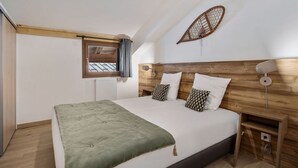 A bedroom with a bed, wooden headboard, a window with curtains, a radiator, and a wall-mounted lamp. - Comfort and Quiet in Nantailly, T3 for 6 pers. (Les Saisies)